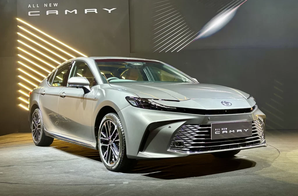 Front view of the 2025 Toyota Camry Hybrid showcased under display lights with a bold new grille and modern LED design